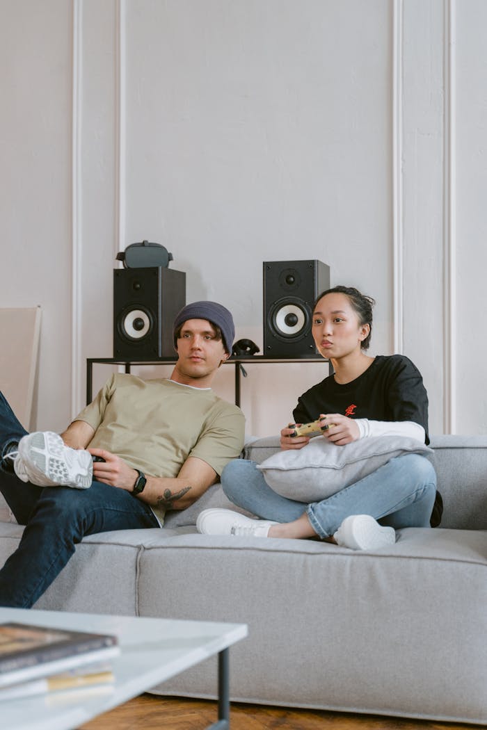Young couple enjoying video games on a modern sofa indoors with gaming consoles.