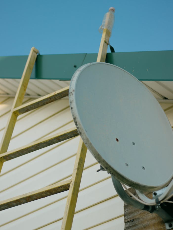 trusted-partner Close-up of a satellite dish and ladder on a house roof against a clear blue sky.